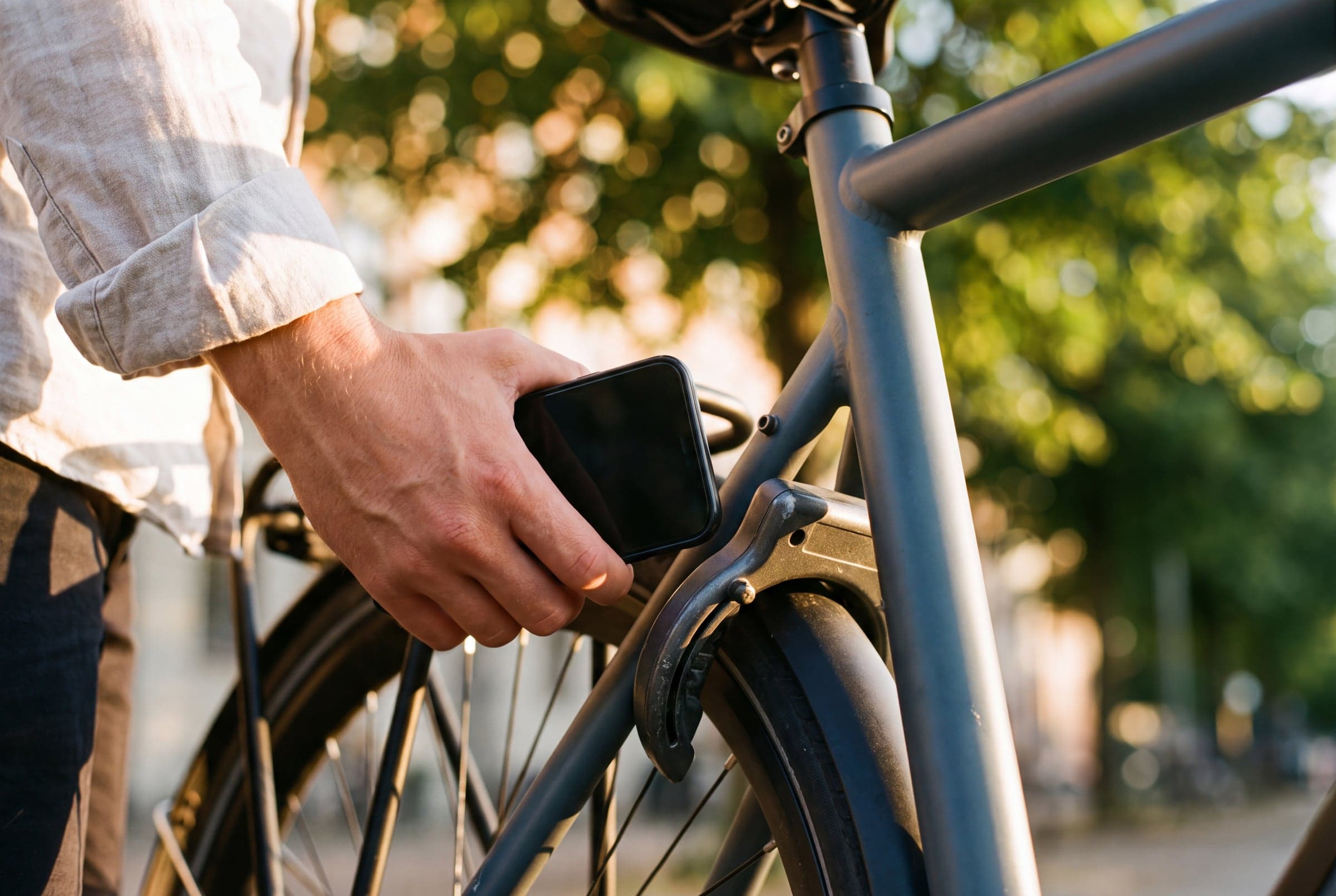 A gloved hand holds a phone beside the frame lock of a Sykla bike on a frosted rack.